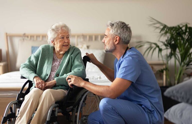 An older adult smiles while talking with a visiting family member in a cozy living room.