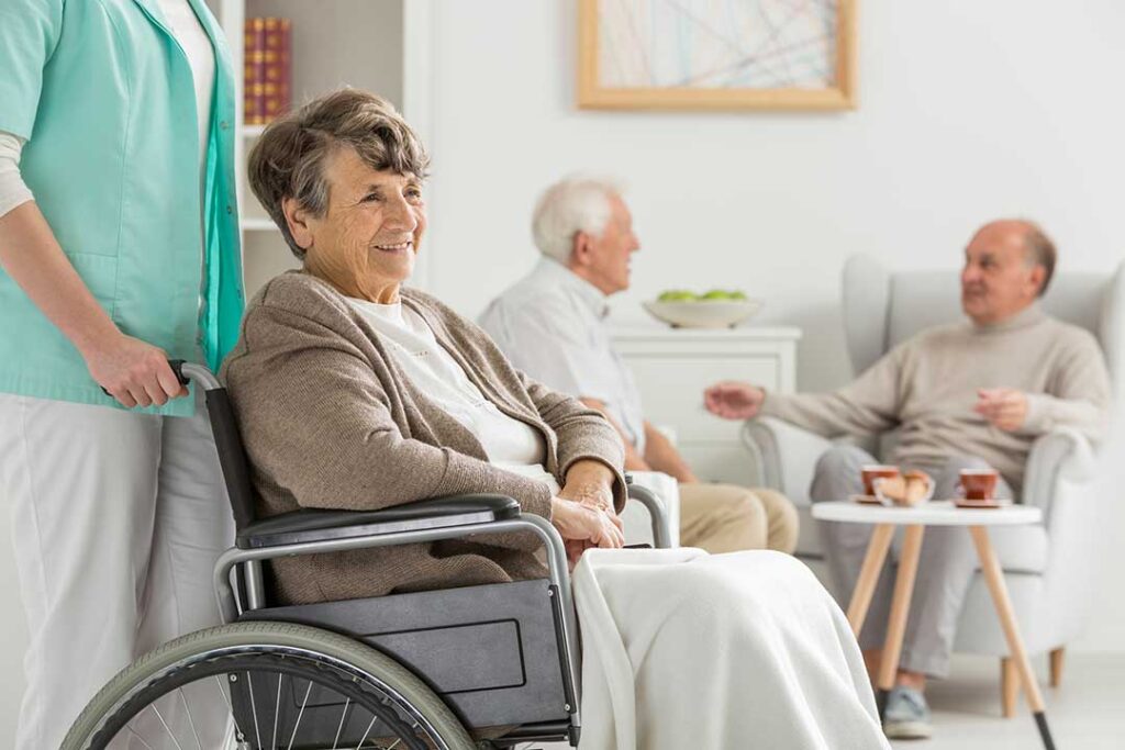 An older adult wearing a personal emergency response device and video calling family on a tablet in a cozy living room.
