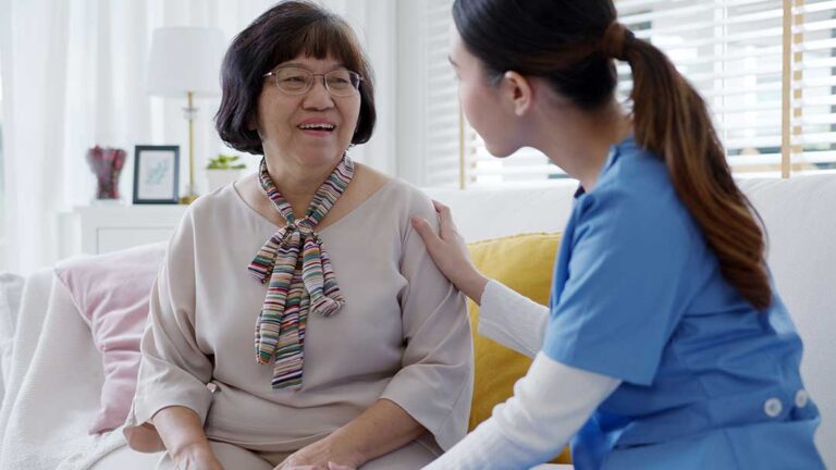A senior adult arranging clothes and keepsakes in a tidy room with sunlight through the window.