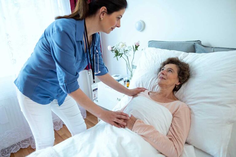 Caregiver reviewing a resident’s medication chart beside an older adult in an assisted living room.